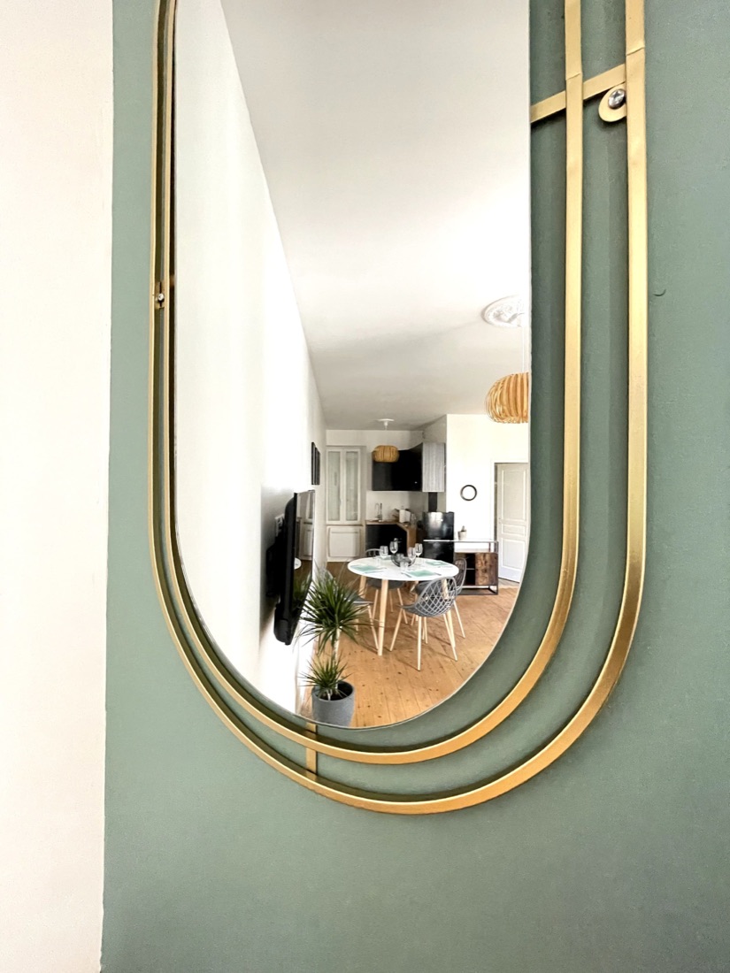 Miroir doré sur mur vert sauge, reflétant la salle à manger